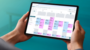 Hände halten ein Tablet mit dem thevea-Wochenkalender, der Patiententermine mehrerer Therapeuten farblich getrennt über fünf Werktage anzeigt.